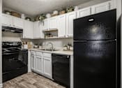 Thumbnail 8 of 14 - A black refrigerator stands in a kitchen with white cabinets and a black stove.