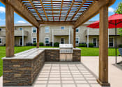 Thumbnail 7 of 20 - A patio with a stone wall and a grill under a wooden pergola.