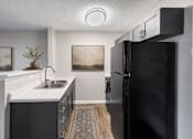 Thumbnail 17 of 20 - A black refrigerator stands in a kitchen with a white counter and a sink.