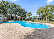 Thumbnail 1 of 28 - A swimming pool surrounded by a brick patio and palm trees. at Epic Apartments , Florida, 32114