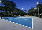 Thumbnail 12 of 28 - Tennis court with blue surface and white lines, surrounded by trees and street lights. at Epic Apartments , Florida, 32114