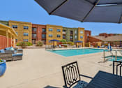 Thumbnail 2 of 10 - A pool area with a table and chairs and a building in the background.