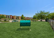 Thumbnail 3 of 10 - A green play structure in a grassy area with apartment buildings in the background.
