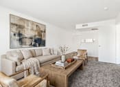 Thumbnail 8 of 10 - A living room with a large painting on the wall and a coffee table in the center.