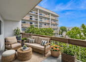 Thumbnail 6 of 12 - A balcony with a sofa, chairs and a table with flowers on it.