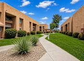 Thumbnail 6 of 23 - A long concrete walkway leads between two rows of tan buildings.