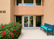 Thumbnail 8 of 23 - A blue bench sits in front of a building with a glass door.