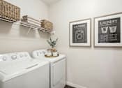 Thumbnail 23 of 25 - A laundry room with a washer and dryer, a shelf with baskets, and two framed laundry instructions at Aster Meadow, Vadnais Heights, MN, 55127