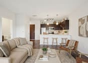 Thumbnail 13 of 25 - A living room with a couch, a chair, a coffee table, and a kitchen area in the background at Aster Meadow, Vadnais Heights, MN, 55127