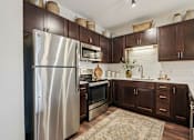 Thumbnail 18 of 25 - A kitchen with a stainless steel refrigerator and wooden cabinets at Aster Meadow, Vadnais Heights, MN, 55127