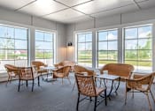 Thumbnail 16 of 41 - Sunroom lounge with wicker chairs and large windows at The Hendrickson Apartments, Falcon Heights, MN