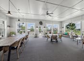 Thumbnail 18 of 41 - Sunroom lounge with ceiling fan and multiple seating areas at The Hendrickson Apartments, Falcon Heights, 55113