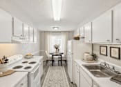 Thumbnail 9 of 16 - A white kitchen with a stove, sink, and dining table.