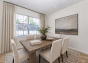 Thumbnail 12 of 17 - A dining room with a wooden table and chairs, a vase with a plant, and a framed picture on the wall.