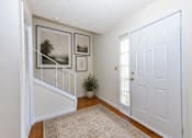 Thumbnail 15 of 17 - A hallway with a white door, a rug on the floor, and pictures on the wall.