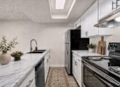 Thumbnail 14 of 26 - Modern galley kitchen with marble countertops at Park Station Apartments, Midvale, UT