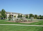 Thumbnail 4 of 23 - A playground with swings and slides in front of apartment buildings.