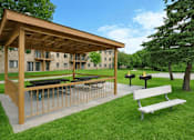 Thumbnail 6 of 23 - A wooden pavilion with a picnic table in front of a building and trees.