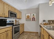 Thumbnail 11 of 14 - Galley kitchen with wood cabinets and modern appliances at Grand Gateway Apartments, St Cloud, 56301
