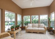 Thumbnail 6 of 20 - A sunroom with a white couch and a ceiling fan.