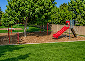 Thumbnail 5 of 17 - A playground with a red slide and a green tree.
