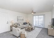 Thumbnail 6 of 7 - A living room with a grey couch, a white door, a ceiling fan, and a television.