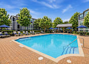 Thumbnail 3 of 17 - A large outdoor swimming pool surrounded by trees and lounge chairs.