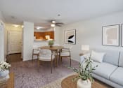 Thumbnail 2 of 22 - A living room with a grey couch, a wooden dining table with four chairs, and a white vase with a plant on the coffee table.