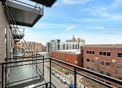 Thumbnail 27 of 36 - A balcony with a metal railing overlooks a parking lot and buildings.