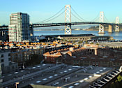 Thumbnail 26 of 40 - A tennis court is situated on a rooftop with a bridge and buildings in the background.