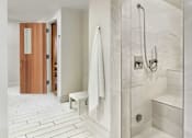 Thumbnail 20 of 40 - A white tiled bathroom with a wooden door and a white bench.