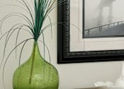 Thumbnail 37 of 40 - A green vase with white pom poms and long thin stems sits on a table.
