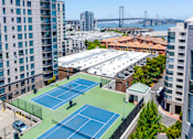 Thumbnail 8 of 95 - Two tennis courts on a rooftop with trees and buildings around.