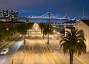Thumbnail 91 of 95 - A city street at night with a bridge in the background.