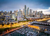 Thumbnail 90 of 95 - A cityscape at dusk with a marina full of boats.