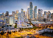 Thumbnail 89 of 95 - A cityscape at dusk with buildings illuminated against a darkening sky.