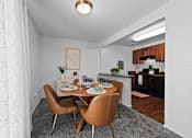 Thumbnail 4 of 20 - A dining room with a table set for two and a kitchen area in the background.