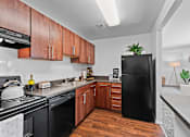 Thumbnail 10 of 20 - A black refrigerator stands in a kitchen with wooden cabinets and a black stove.