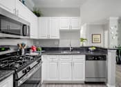 Thumbnail 15 of 42 - A modern kitchen with white cabinets and a black countertop at The Grand Reserve at Tampa Palms Apartments, Tampa, Florida