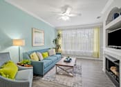Thumbnail 5 of 42 - A living room with a grey couch, a green chair, a coffee table, a fireplace, and a ceiling fan at The Grand Reserve at Tampa Palms Apartments, Tampa, FL