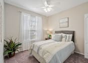 Thumbnail 10 of 42 - A bedroom with a bed, a potted plant, and a ceiling fan at The Grand Reserve at Tampa Palms Apartments, Florida, 33647