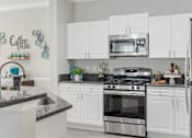 Thumbnail 1 of 42 - A kitchen with white cabinets and a black countertop at The Grand Reserve at Tampa Palms Apartments, Tampa
