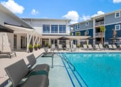Thumbnail 9 of 15 - a swimming pool with lounge chairs and umbrellas in front of a building at Bristol at New Riverside, Bluffton, SC 29910