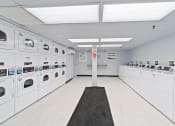 Thumbnail 12 of 14 - Community laundry center with white washers and dryers and a black rug on the floor at Mount Ridge Apartments, Baltimore, MD