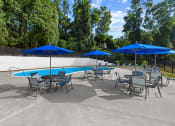 Thumbnail 11 of 12 - a group of tables with umbrellas and chairs around a pool at Brook View Apartments, 21209, MD