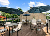Thumbnail 6 of 20 - an outdoor patio with tables and chairs and umbrellas at McDonogh Township Apartments, Owings Mills, Maryland