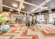 Thumbnail 12 of 18 - a gym with a variety of exercise equipment and a large window at Dartmoor Place at Oxford Square Apartments, Hanover, MD