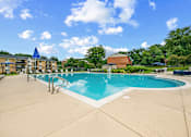 Thumbnail 17 of 26 - A large outdoor swimming pool with a blue sky and clouds in the background.