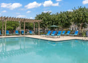 Thumbnail 24 of 41 - a swimming pool with blue chaise lounge chairs and a pergola with trees in the at Fortress Grove, Murfreesboro