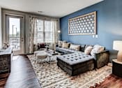 Thumbnail 5 of 16 - A living room with a dark brown sofa and a tufted ottoman at The Linden Apartments, Davidson, NC